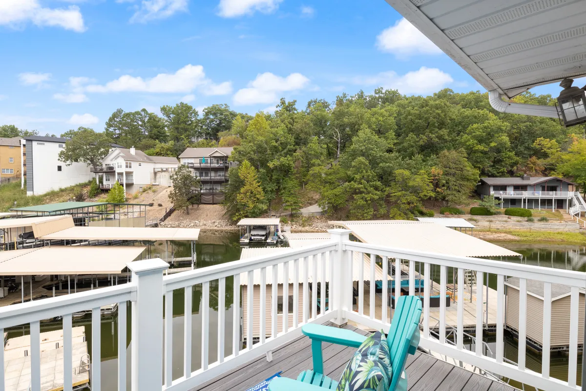 A peaceful lakeside view highlighting the dock area, calm water, and surrounding trees with houses nestled on the hillside. The dock is ideal for launching paddle boards, docking boats, or simply relaxing by the water.