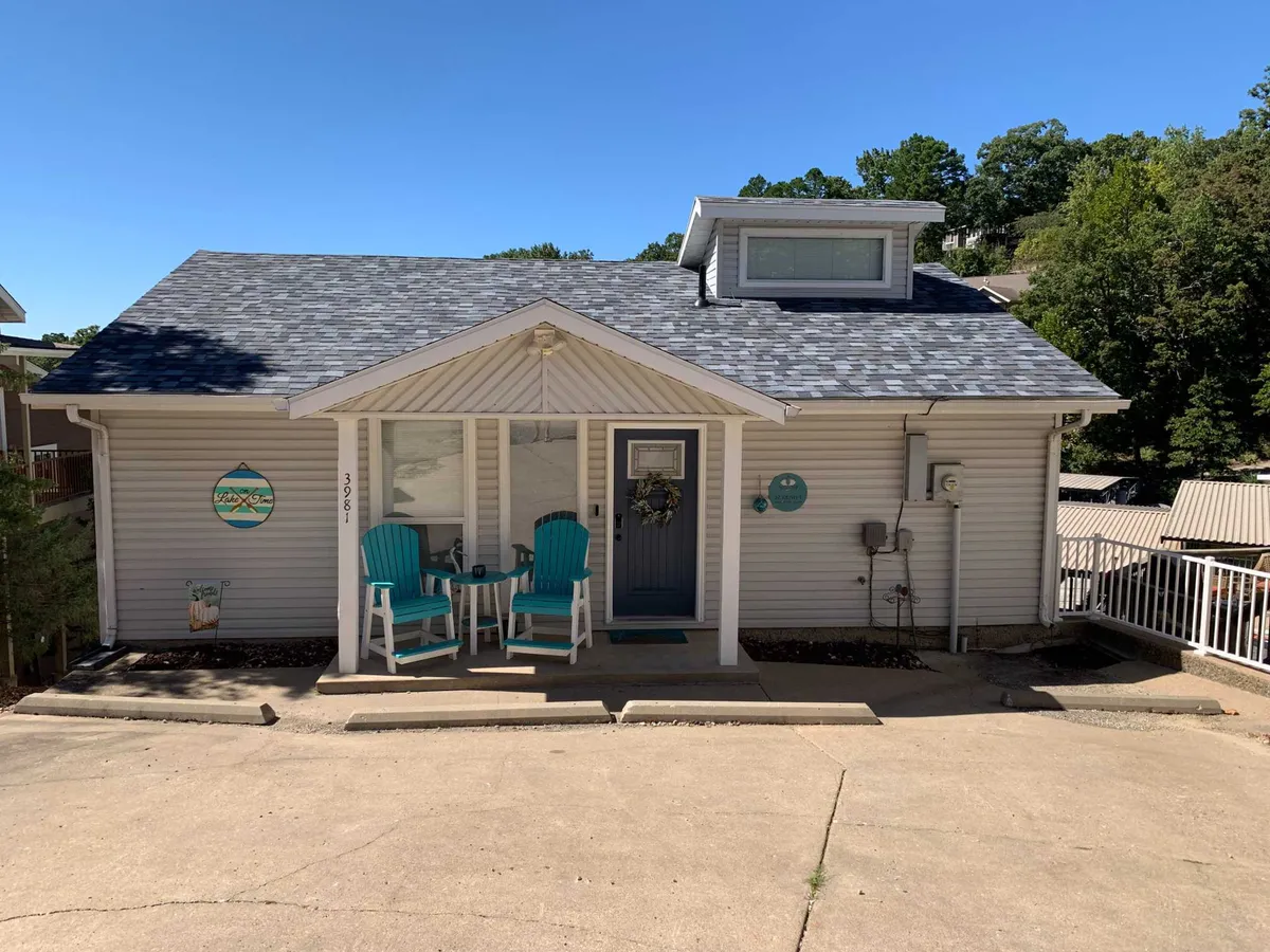 A welcoming front porch with two turquoise chairs, a decorative wreath, and a blue door adorned with charming details. The porch is an inviting space suggesting relaxation and connection to the peaceful outdoor environment.
