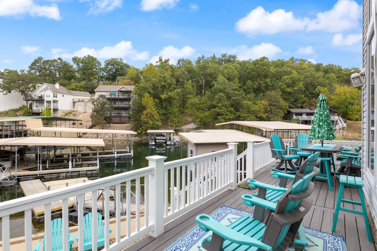 A private dock extends over calm lake waters, with boats moored nearby and an outdoor seating area nestled among green trees under a blue sky. The scene evokes peaceful afternoons spent fishing, swimming, or simply relaxing by the water’s edge.