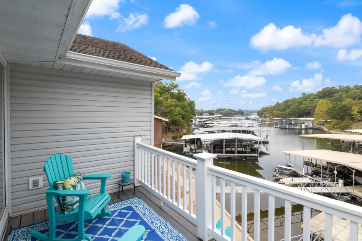 A tranquil exterior scene with a blue Adirondack chair and decorative rug facing the water, with docks and boats visible in the background. The setup is ideal for soaking in the lakeside views, reading, or enjoying a drink while being close to the action on the water.
