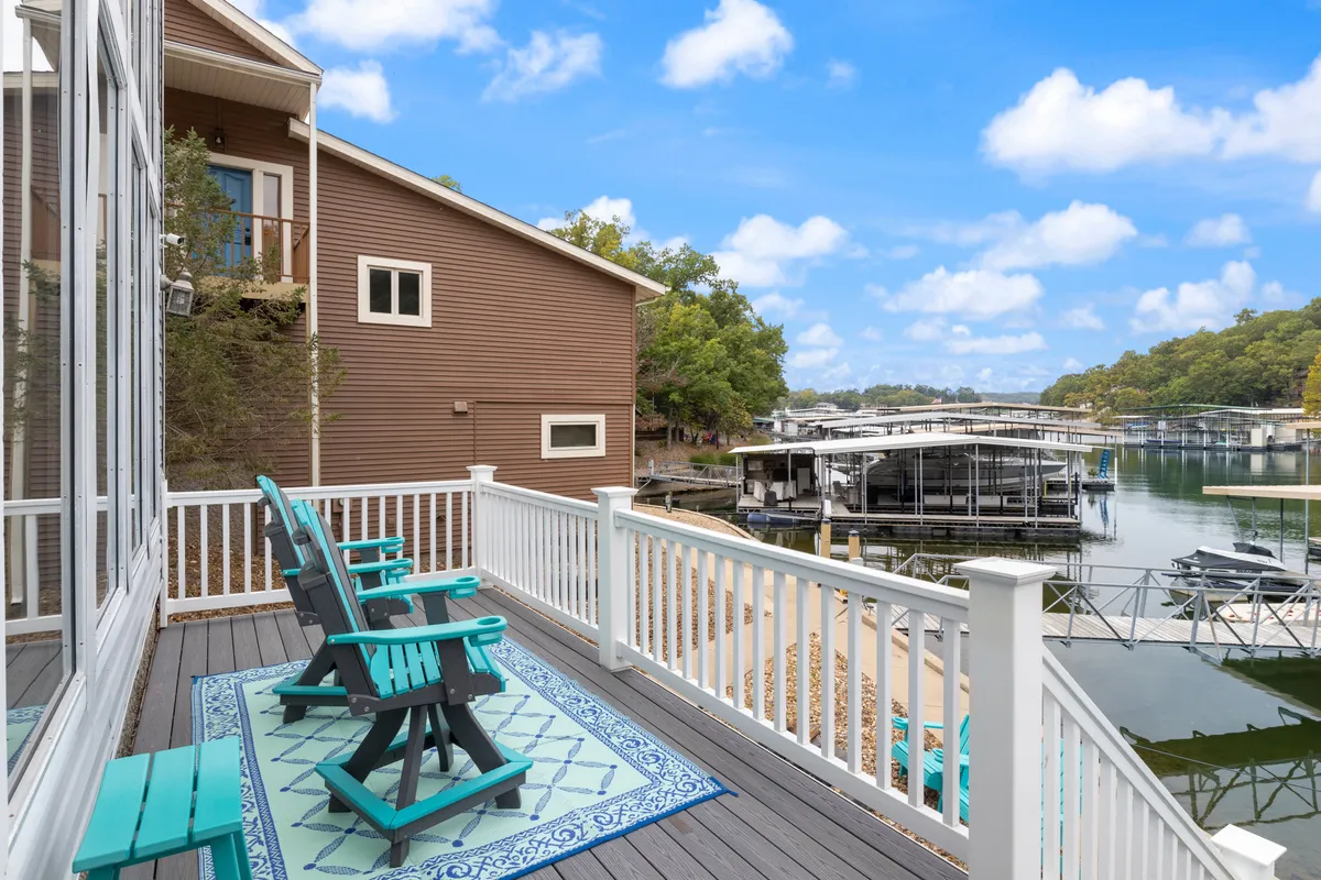 A serene exterior deck scene featuring comfortable deck chairs with an area rug, all overlooking a private dock that extends into the calm lake waters. The setting is perfect for relaxing, socializing, or preparing for aquatic adventures right from the dock.