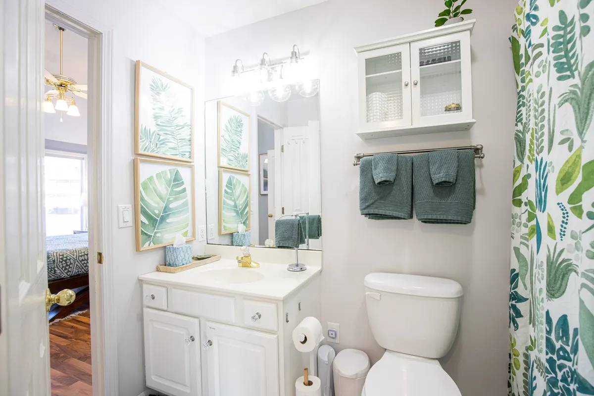 A calming bathroom scene with framed leaf artwork, a large mirror reflecting gentle light, and green towels neatly hung, creating a sense of a fresh and rejuvenating space ideal for morning routines.