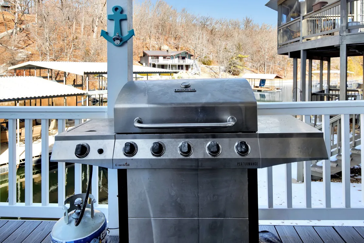 An exterior shot of a stainless steel grill with a blue anchor decor and propane tank, set up for outdoor cooking. The setting is relaxed and ready for lakeside barbecues or evening gatherings.