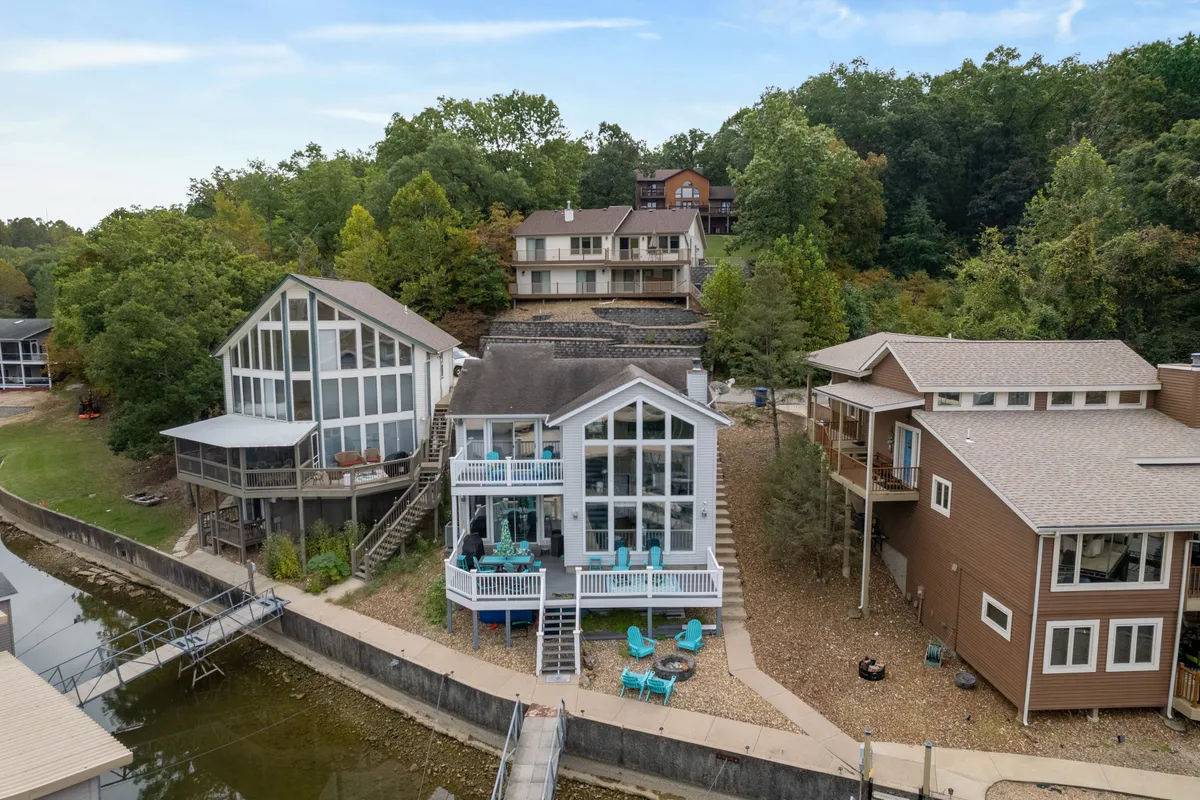 A spacious lakefront deck with comfortable seating overlooks tranquil waters, framed by modern architecture and lush greenery. The open and inviting outdoor space suggests room for social gatherings and family activities, with a clear view of the lake just steps away.