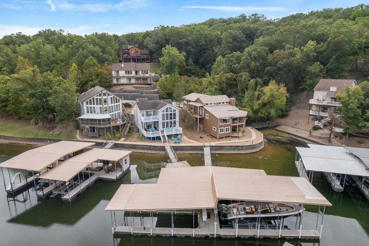 A scenic exterior shot showing modern lakeside homes with private docks, lush greenery, and calm water. The space is perfect for gatherings by the water, with potential for bonfires, fishing, and group relaxation at sunset.
