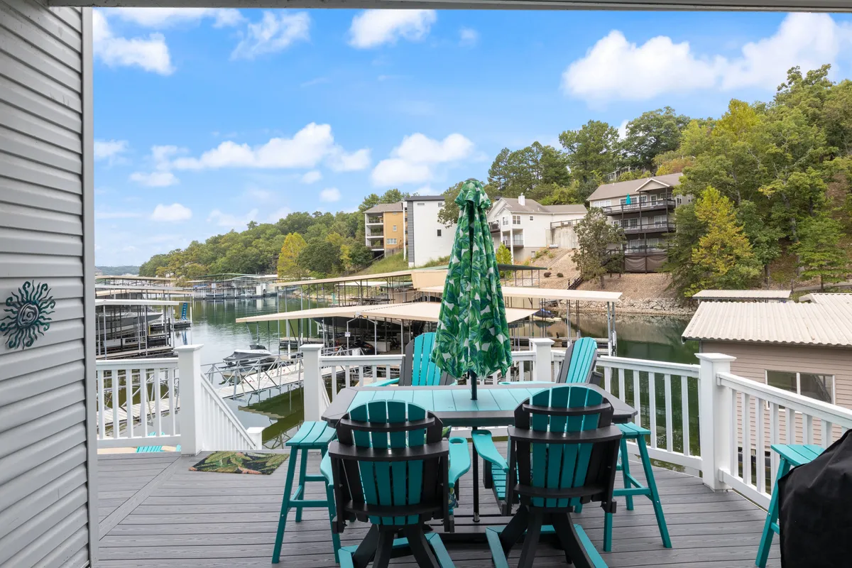 A welcoming outdoor dining area with a green umbrella and a view of the lake and marina beyond. The setup includes a spacious table, lush greenery, and easy access to the water, evoking a sense of relaxation and sociability in a beautiful natural context.