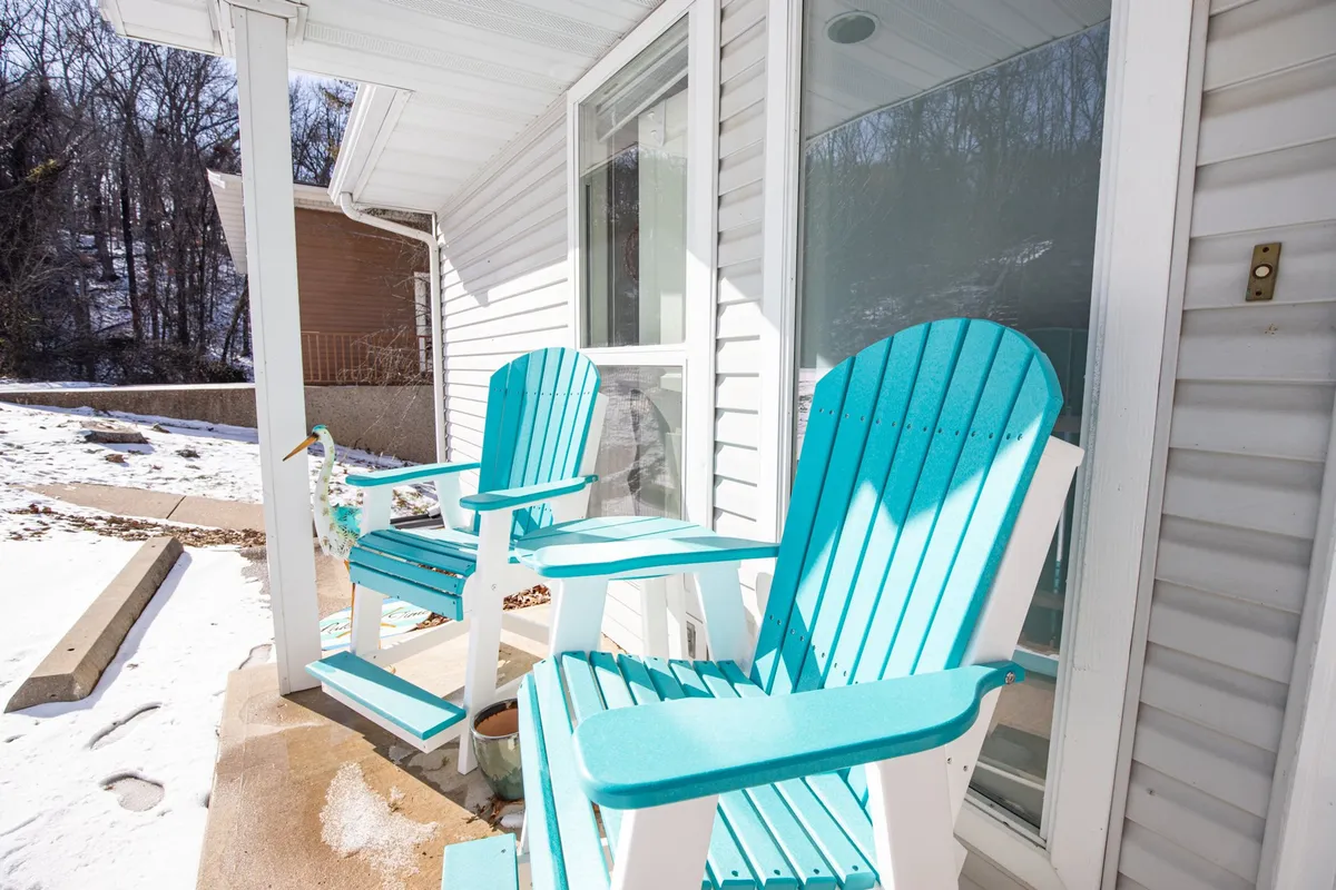 The calm front porch scene features two turquoise chairs and views of surrounding trees, suggesting a peaceful transition between indoor comfort and the natural world outside. The area feels serene and welcoming—an ideal spot for unwinding or keeping an eye on a pet in the yard.